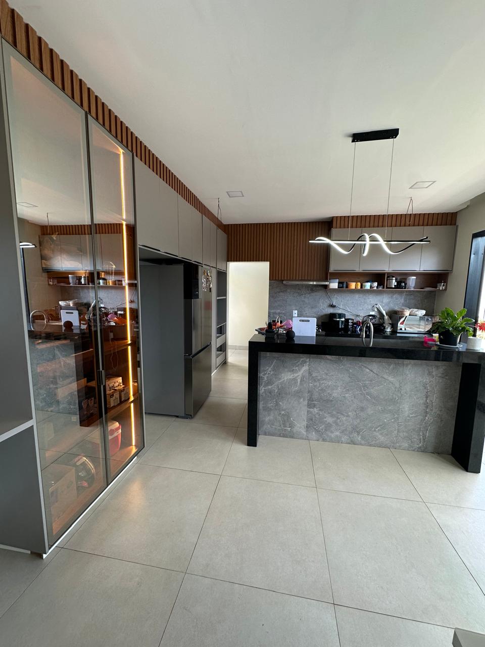 Cozinha planejada com vitrine de vidro iluminada, ripado de madeira no teto e bancada com revestimento em pedra